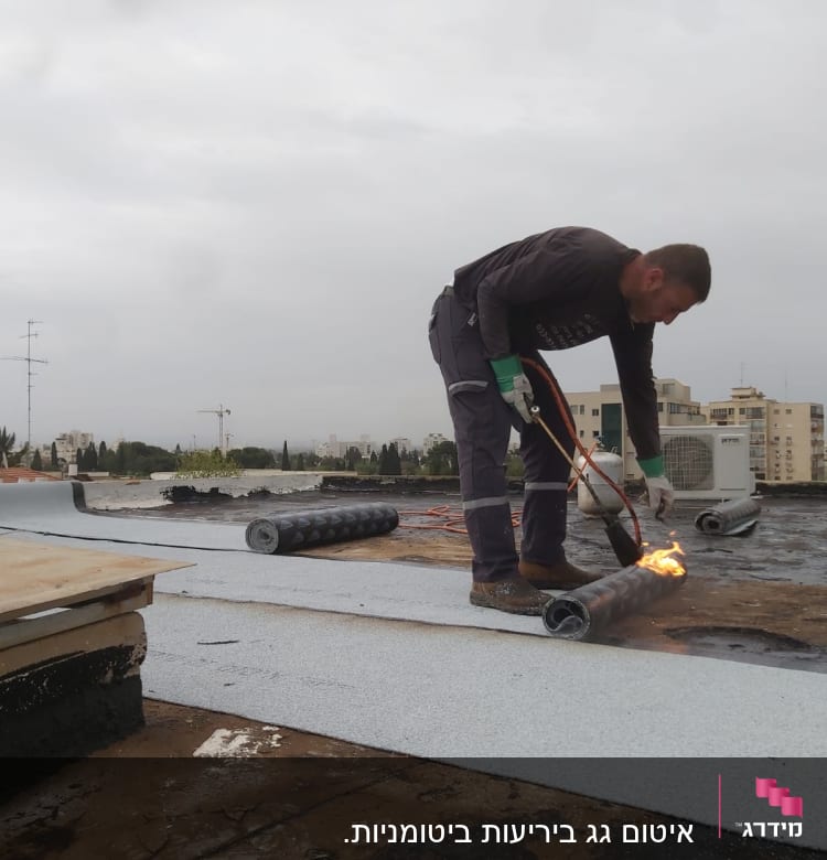 אדם מחמם יריעות איטום על גג עם מבער